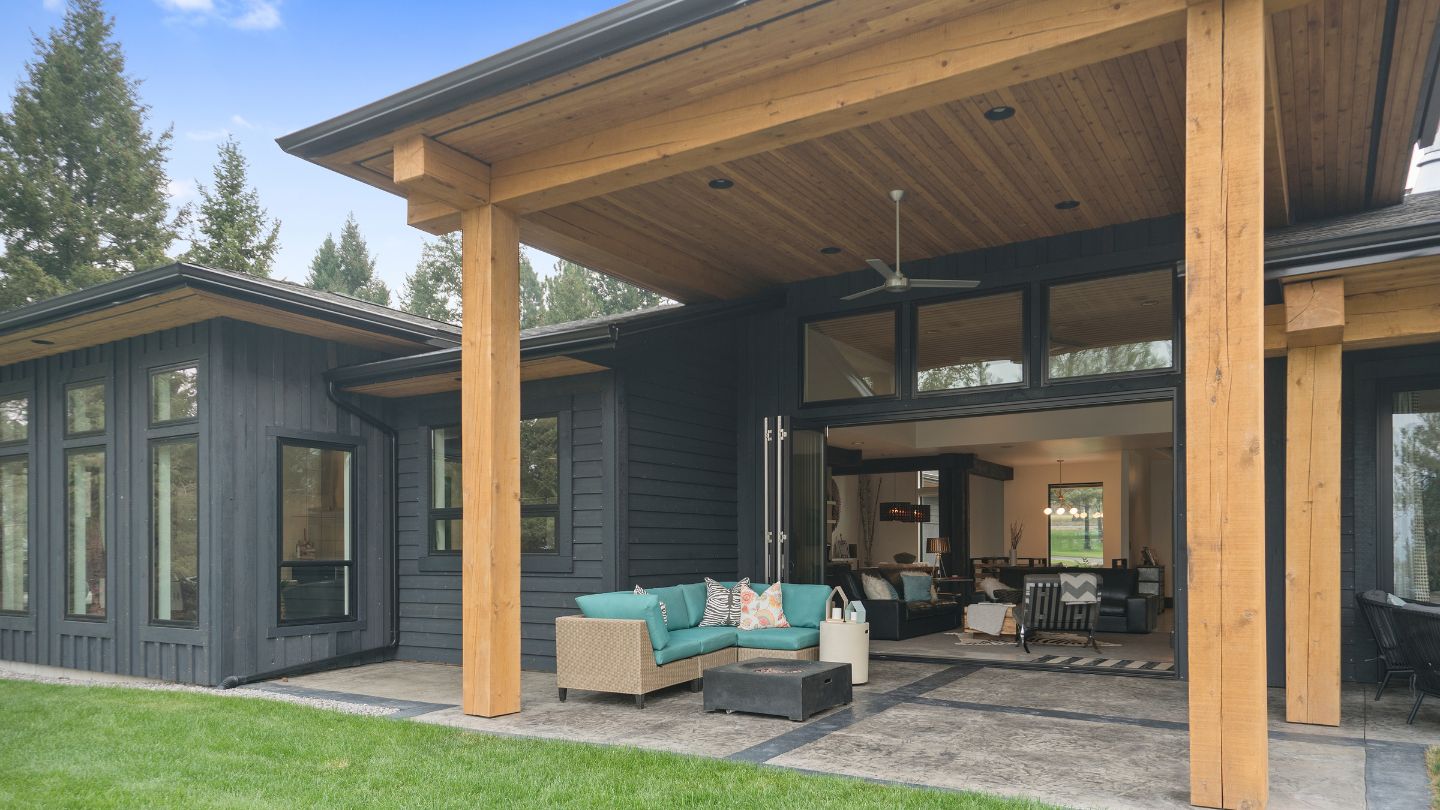 Residential home in a backyard setting featuring artificial grass, with a covered patio and outdoor seating area.