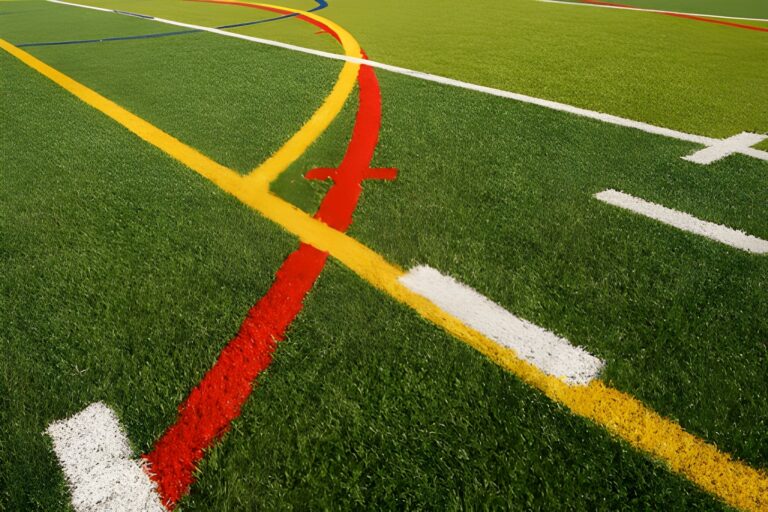 A detailed, close-up view of green athletic turf painted with crisscrossing boundary lines in white, yellow, red, and blue.