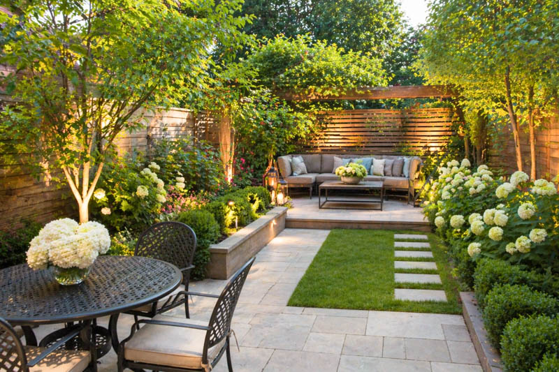 Landscaped backyard patio with a stone path, sectional sofa, and white hydrangea bushes.